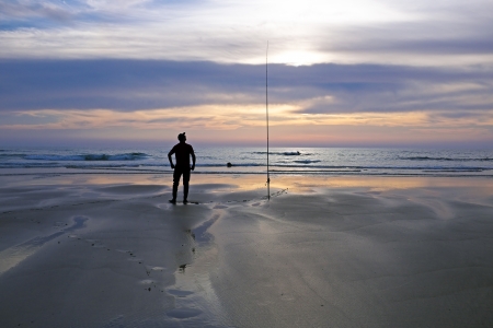 Lonely fisherman at the beach at twilightの写真素材
