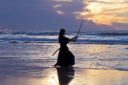 Young samurai women with Japanese sword(Katana) at sunset on the beachの写真素材