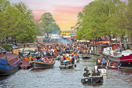AMSTERDAM - APRIL 26: Amsterdam canals full of boats and people in orange during the celebration of kings day on April 26, 2014 in Amsterdam, The Netherlands at sunsetのeditorial素材