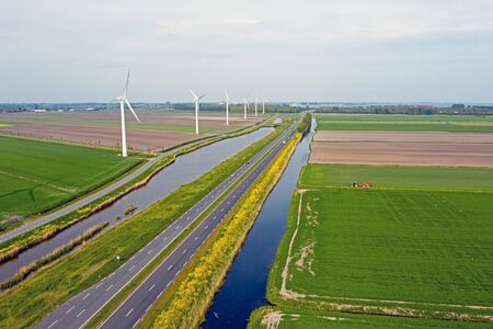 Aerial from a typical dutch landscape: Wind turbines, canals, straight roads and flat meadows in the countryside from the Netherlandsの写真素材