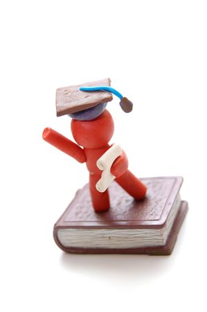 Plasticine figure celebrating graduation with certificate and student hat staying on bookの写真素材