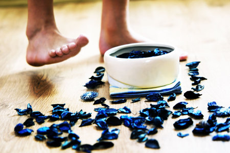 Spa therapy. Flower petals in bowl, on the floor and legs in the backgroundの写真素材