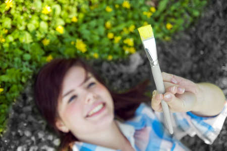 Painting the world. Smiling girl on grass with a paintbrushの写真素材