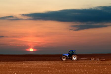 Agriculture scenery, tractor working at sunsetの写真素材