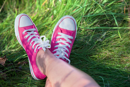 Pink sneakers on girl legs on grass during sunny summer day.