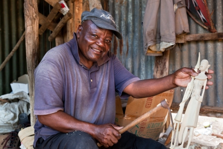 Southern part of KENYA, AFRICA - DECEMBER 10: A man carving figures in wood. Thousands of Africans in Kenya live on souvenirs handcraft. December 10, 2012 on the back of the souvenirs shop by the roadside in southern Kenya.のeditorial素材