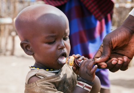Maasai village, TANZANIA, AFRICA - DECEMBER 11: Maasai child trying a Chupa Chups lollipop which has been given by tourists on December 11, 2012 in Ngorongoro Tanzania. Maasai people live their traditional uncivilized way and sometimes tourist offer them のeditorial素材