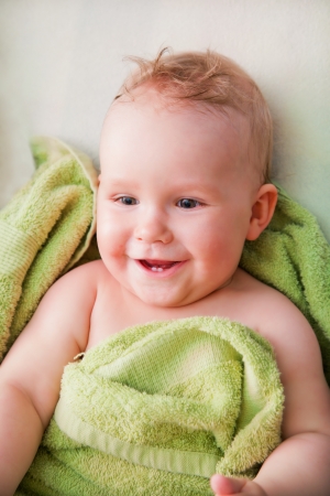A happy smiling baby lying on bed in green towelの写真素材