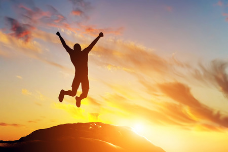 Happy man jumping for joy on the peak of the mountain, cliff at sunset. Success, winner, happinessの写真素材
