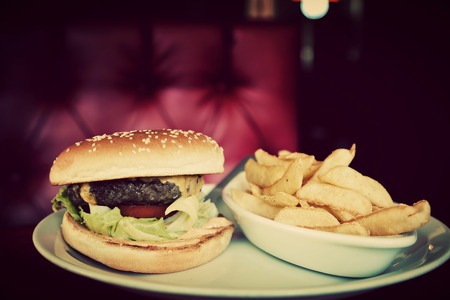 Tasty hamburger and french fries on plate in american food restaurant. Red leather sofa in the background. Vintage, retro styleの写真素材