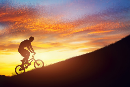 Man riding a bmx bike uphill against sunset sky. Active lifestyle, motivation, strength, challengeの写真素材