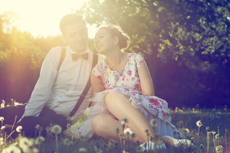 Romantic couple in love flirting on grass in sunny spring park. Dating, vintage romance, sun flare.の写真素材