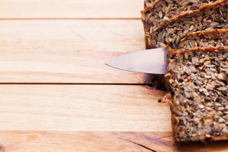 Knife in wholemeal, wholewheat bread on wooden table. Organic, healthy food, breakfast. Top view.