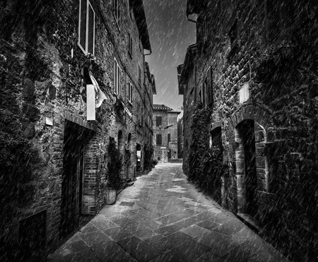Dark narrow street in an old Italian town in Tuscany, Italy. Raining, black and whiteの写真素材