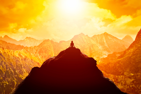 Woman meditating in sitting yoga position on the top of a mountains above clouds at sunset. Zen, meditation, peace