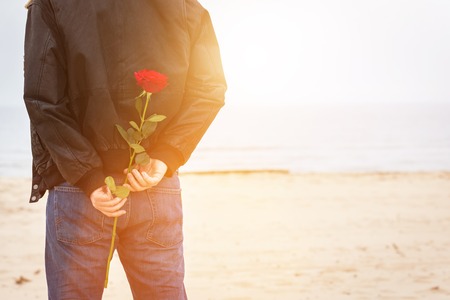 Man with a rose behind his back waiting for love. Date on the beach. Romantic surpriseの写真素材