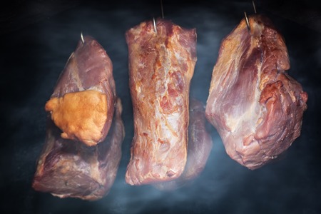 Pork meat hanging on hooks in smoke. Preparing smoked ham. Organic home-made food.の写真素材