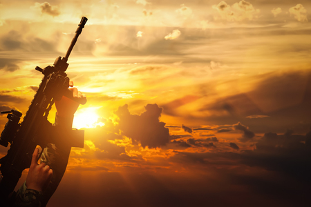 Soldier in combat shooting with his weapon, rifle at sunset. War, army, military.の写真素材