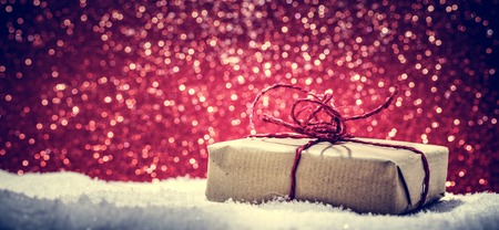 Retro rustic Christmas gift, present in snow on glitter background. Handmade eco paper wrap.の写真素材