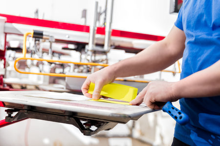 Man preparing material for screen printing in a workshop. Serigraphy industry. Manufacture work.