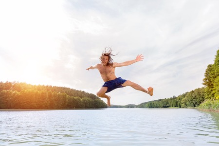 Young fit man making a jump into a lake. Nature and summer activity. Water sport.の写真素材