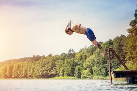 Young fit man jumping into a lake from a wooden jetty. Water sport. Side view.の写真素材