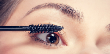 Eye makeup application. Close-up shot of a young woman applying mascara to her lashes.の写真素材