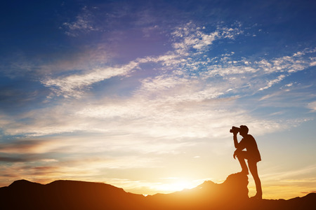 Man standing on rocks, looking through binoculars. Looking forward into the future. Sunset scenic sky. 3d illustration.の写真素材