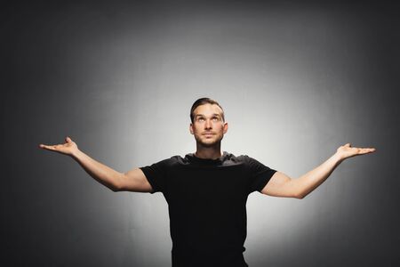 Young handsome man spreading his hands and looking up. Studio portrait.の写真素材