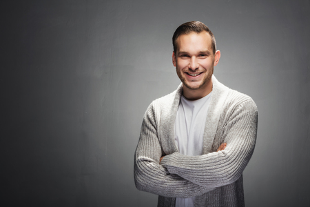 Charming young brunet man in a warm, cozy sweater looking friendly and smiling. Studio portrait.の写真素材