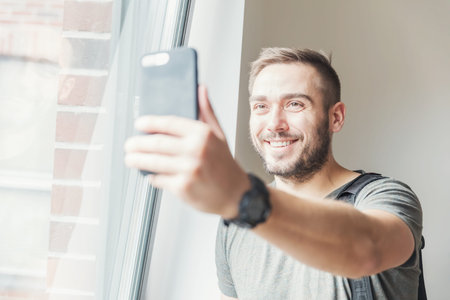 Fit millenial man taking a selfie in the daylight, holding a phone in his hand.