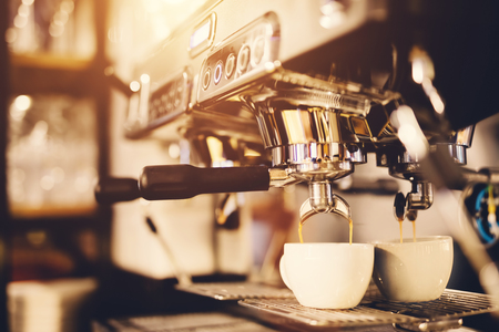 White cup standing beneath a coffeemaker, coffee pouring into it. Morning beverage preparation.の写真素材