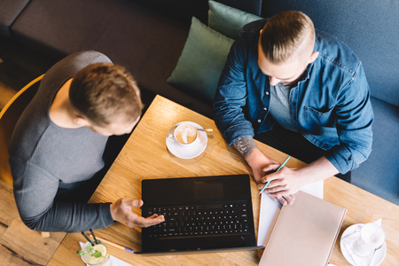 Two men working in a cafe. Documents, laptop, notebook and drinks on the table. View from the top.の写真素材