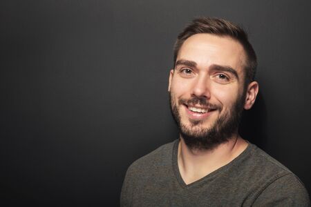 Good-looking dark-haired man in his 30s smiling and looking happy. Casual portrait on black backgroundの写真素材