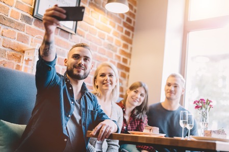 Group of people taking a selfie together in a restaurant. Modern days gadgets. Group picture.の写真素材