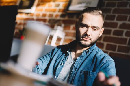 Serious young man sitting in a cafe, looking focused. Coffee in the foreground. Millennial lifestyle.の写真素材