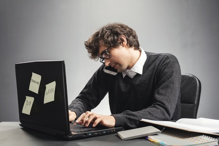 Young working man, typing on the keyboard and talking on the phone. Office work concept.の写真素材