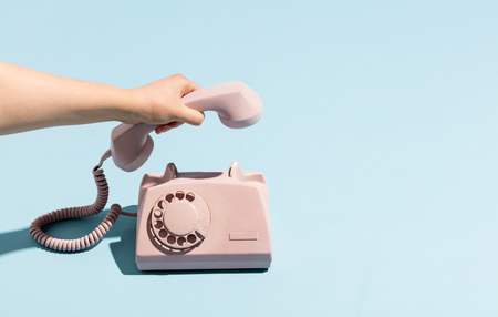 Woman's hand putting a retro telephone reciver down, hanging up. Pastel colors. Blue and pink.