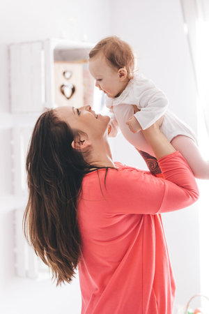 Young woman lifting her baby daughter up. Parenthood concept. Raising a child.