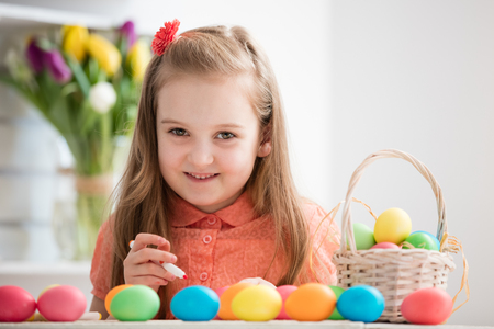 Young girl painting eggs by the desk, smiling. Easter eggs. Christian traditions.の写真素材