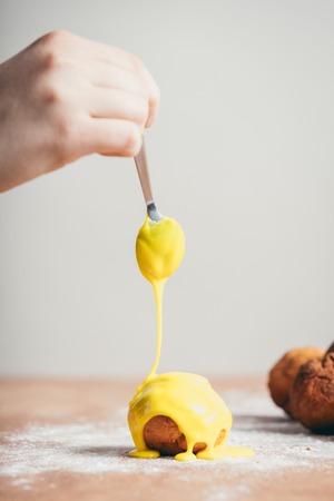 Woman's hand coating a doughnut with yellow frosting. Homemade delicious foods.の写真素材