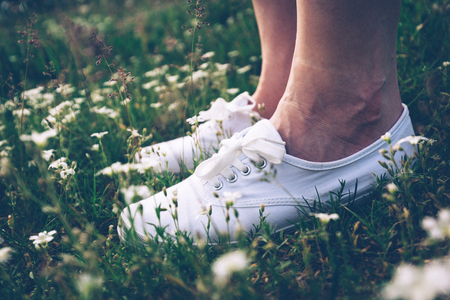 Woman in white sneakers standing on spring meadow with flowers. Feet close-up. Vintage.の写真素材