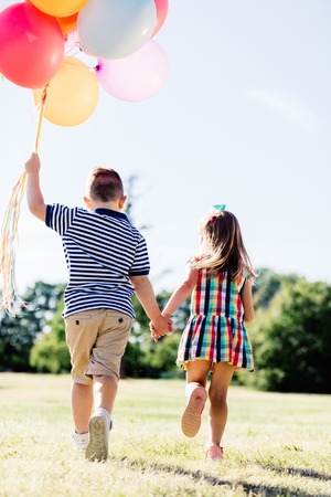 Young boy and a girl running in the park with a bunch of colorful balloons. Children. Valentine's Day.の写真素材