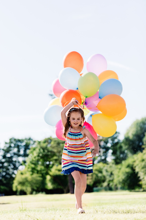 Happy little girl running with a bunch of colorful balloons in the park. Children's party.の写真素材