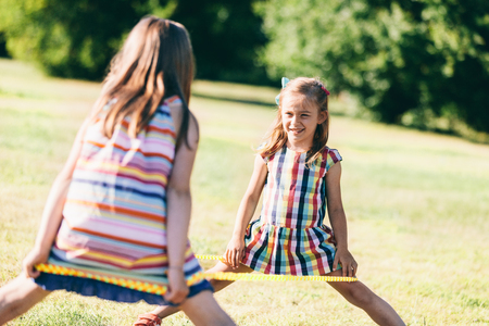 Two girls standing with an elastic wrapped around their legs. Childhood games.の写真素材