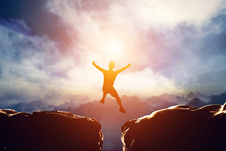 Man jumping for joy between two mountains at sunset. Concept of challenge, taking a risk, having...