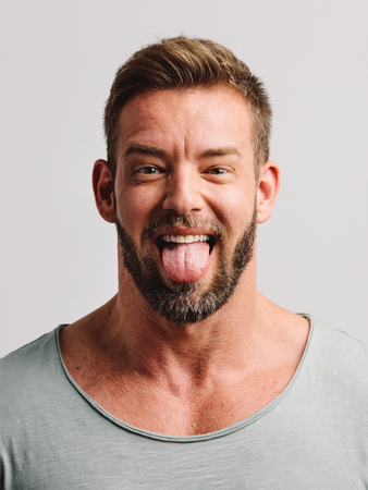 Handsome man sticking his tongue out making faces. Close-up casual portraitの写真素材