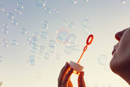 Young woman blowing bubbles to the sky at sunset. Carefree summertime, holidaysの写真素材