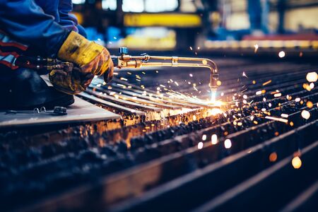 Worker cutting metal, steel with acetylene torch in big factory. Heavy industry, shipyardの写真素材