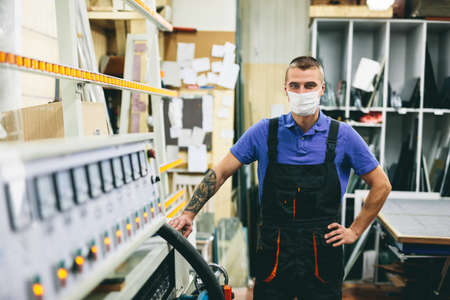 Glazier worker in face mask operates glass cutting machine in workshop. Industry during coronavirus Covid-19の写真素材